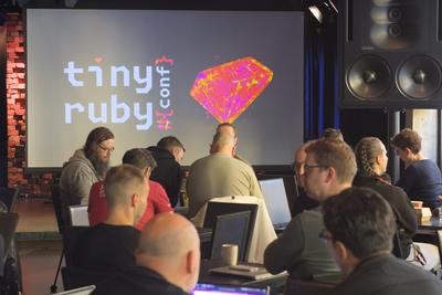 The tiny ruby conf logo on the big screen with attendees in front
