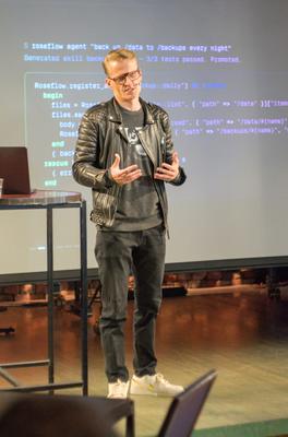 Lauri on stage in front of a code slide